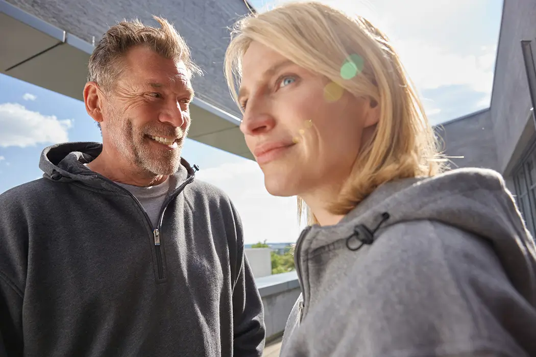 Mann und Frau mit Daiber Kapuzen Sweatshirt JN839, stehen draußen, Detail auf kurzer Reißverschluss – Lifestyleaufnahme