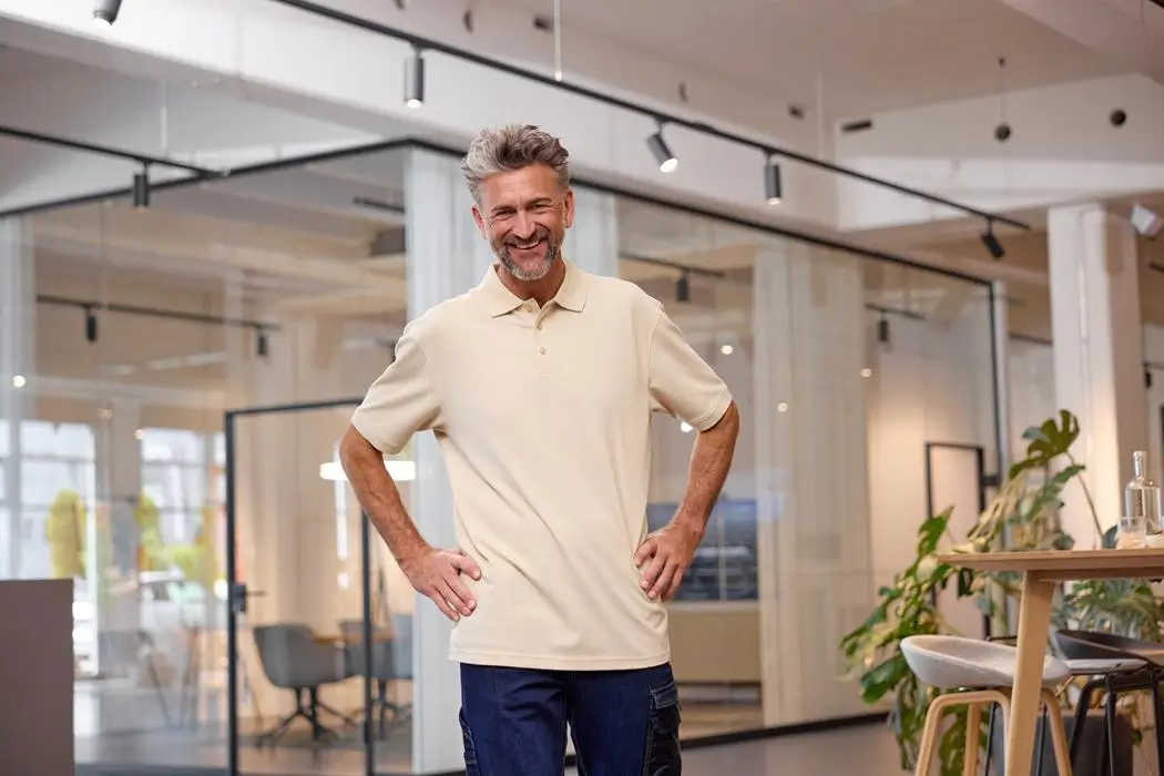 Daiber Herren kurzarm Poloshirt JN874 stone Mann trägt kurzarm Poloshirt JN874 in der Farbe stone, stehen in einem Großen Raum, Lifestyleaufnahme