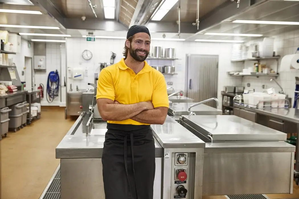 Daiber Herren kurzarm Poloshirt JN874 goldgelb Mann trägt kurzarm Poloshirt von Daiber in limegrün, stehend in der Großküche, Lifestyleaufnahme