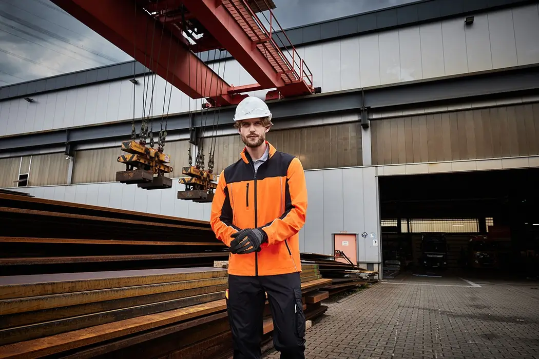 Handwerker auf der Baustelle, trägt Arbeitsjacke in neonorange-schwarz bei der Arbeit