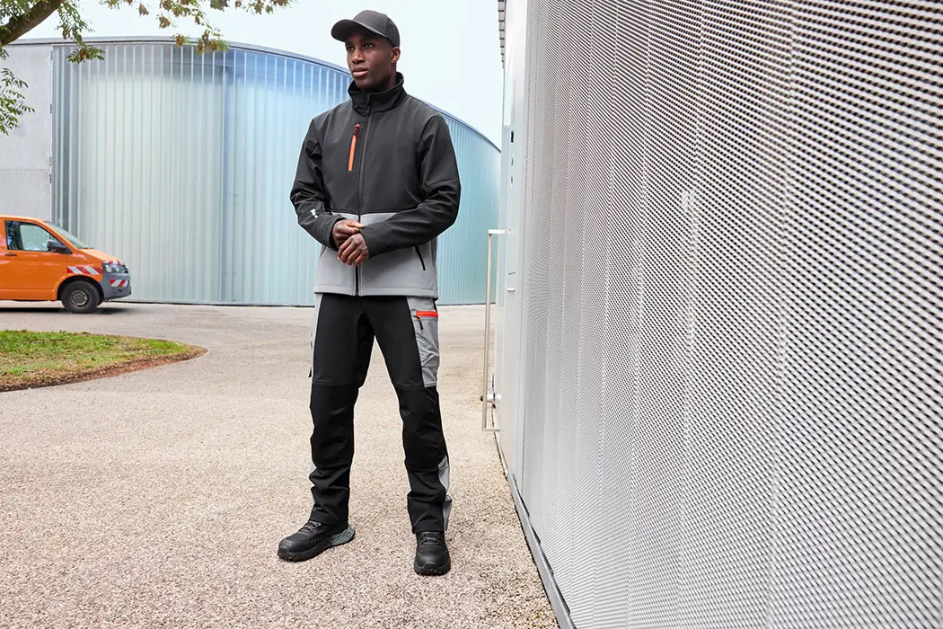 Daiber Workwear Softshelljacke JN1886 Unisex in black/metal-grey getragen von einem Mann vor einer Lagerhalle