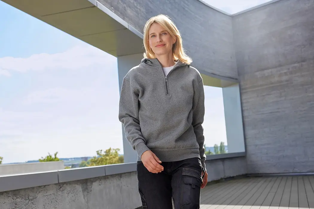 Frau trägt hellgraues Kapuzen Sweatshirt und geht draußen auf Terrasse – Lifestyleaufnahme