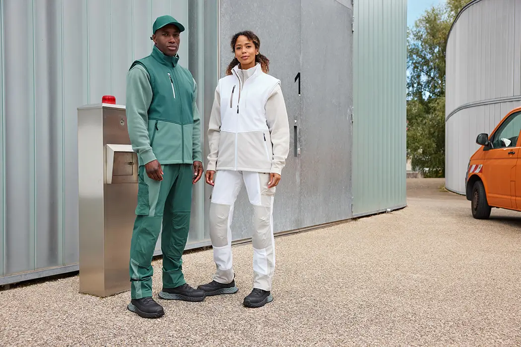 Daiber Workwear Softshellweste JN1888 in weiss von Damen und grün von Herren getragen vor einer Lagerhalle