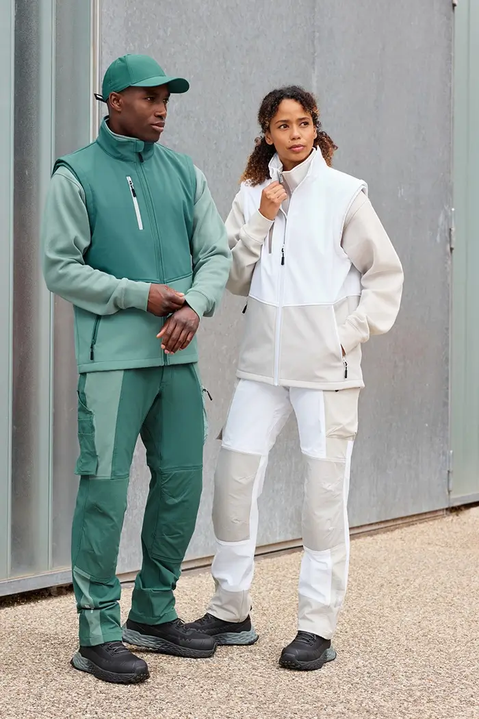 Daiber Workwear Softshellweste JN1888 von Damen in weiss und von Herren in grün getragen vor einer Lagerhalle