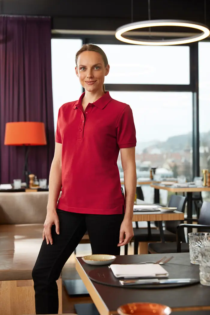 Daiber Damen Poloshirt JN873 rot Frau trägt Poloshirt in der Farbe rot bei der Arbeit als Bedinung, Lifestyleaufnahme