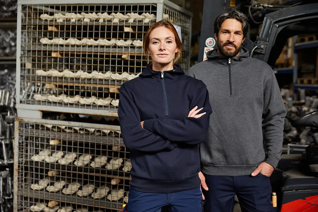 Frau und Mann stehend mit Kapuzen Sweatshirt in navy und dunkelgrau in der Bäckereifertigung